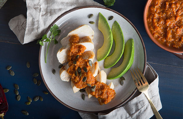 Sliced chicken topped with a butternut squash mole with pepitas and avocado garnish.